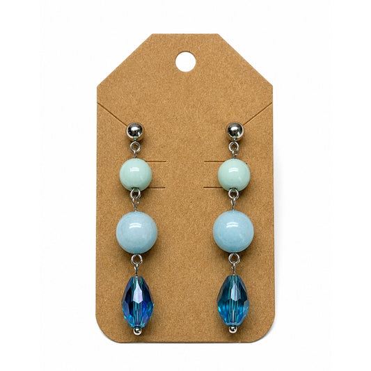 A pair of drop earrings displayed on a brown kraft card. Each earring has three stacked round beads in pale mint green, light blue, and deep blue, finished with a faceted blue teardrop bead at the bottom and silver-tone posts.