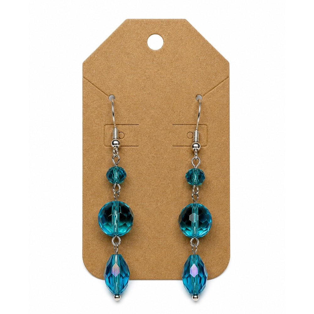 A pair of dangling earrings with faceted teal-blue beads on silver hooks, displayed on a brown kraft card against a white background.