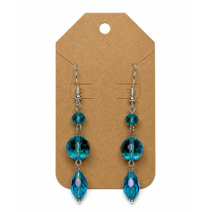A pair of dangling earrings with faceted teal-blue beads on silver hooks, displayed on a brown kraft card against a white background.